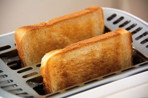Zwei goldbraun geröstete Toastbrotscheiben stecken in den Schlitzen eines weißen Toasters | Sabine Verheyen