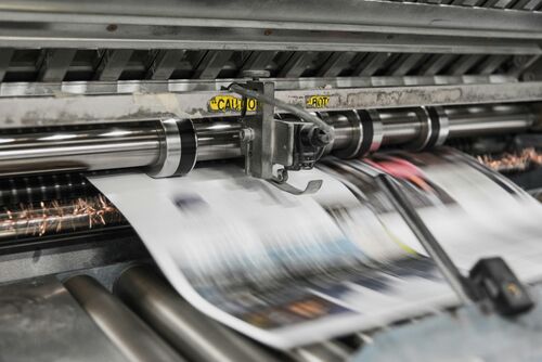 Nahaufnahme einer rotierenden Druckerpresse, durch die in hoher Geschwindigkeit Papier läuft | Sabine Verheyen
